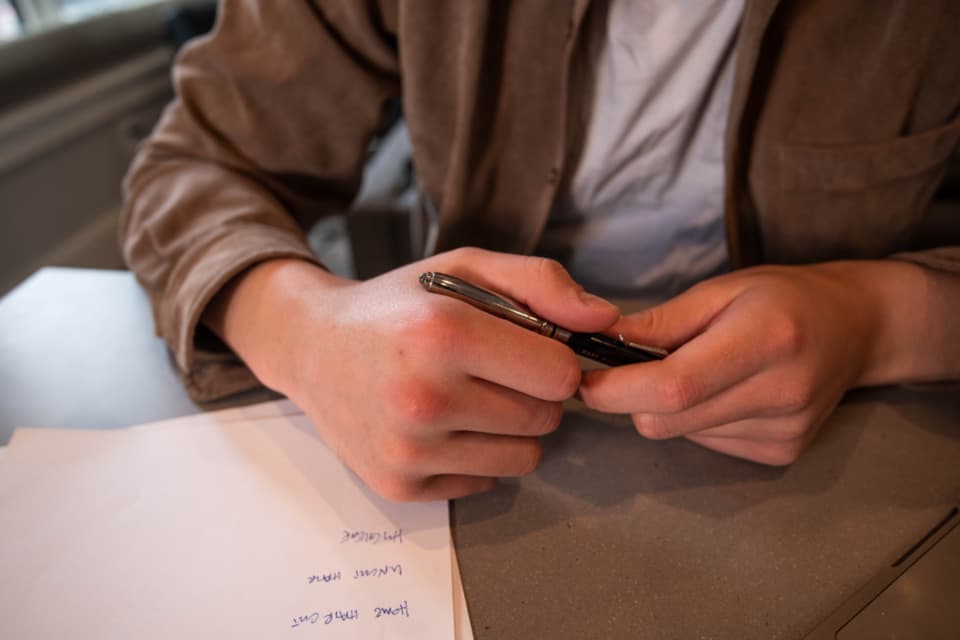 Mains tenant un stylo au-dessus d'un document manuscrit, sur un bureau